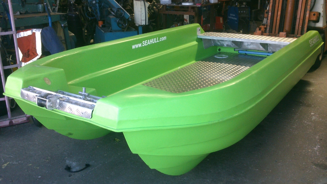 A bright green Sea Bullet boat displayed indoors, showcasing its hull design and aluminum deck under workshop lighting.
